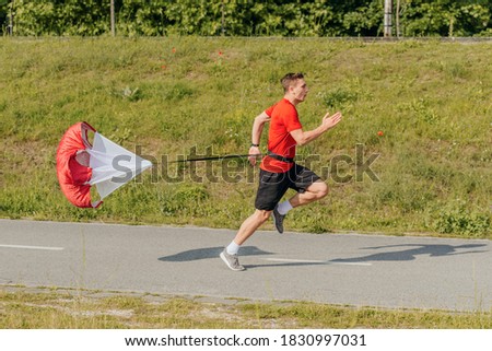 Side view of a strong man doing workout using resistance parachute outdoors