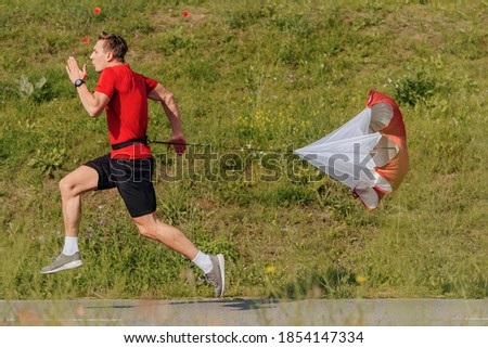 Side view of a strong man doing workout using resistance parachute outdoors