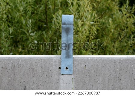 Side view of strong metal safety guard rail holder mounted without screw on top of concrete road bridge barrier covered with cobweb and dust on warm summer day with trees in background