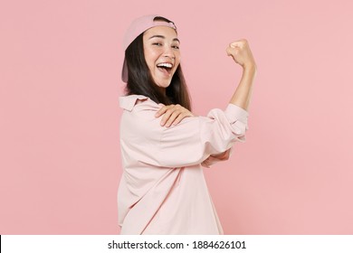 Side view of strong young asian woman 20s in casual clothes cap posing isolated on pastel pink background studio portrait. People emotions lifestyle concept. Mock up copy space. Showing biceps muscles
