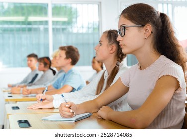 Side view of student group working on lecture in classroom, making notes