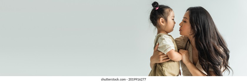 Side View Of Stylish Asian Mother Hugging Toddler Daughter Isolated On Grey, Banner