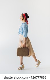 Side View Of Stylish Asian Woman Walking With Suitcase In Hand Isolated On Grey