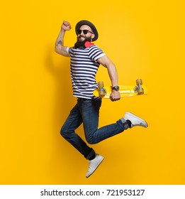 Side view of stylish hipster man with cruiser board jumping on colorful yellow background. - Powered by Shutterstock