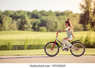 Side View Of Stylish Little Girl In Sun Glasses Riding Bike Outdoors