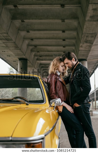 side view of stylish young couple hugging near\
yellow old-fashioned\
automobile