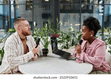 Side view of successful Black woman hosting podcast interviewing businessman while recording broadcast session at cafe table equipped with professional microphones, copy space - Powered by Shutterstock