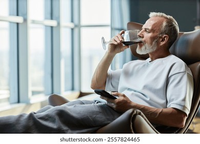 Side view of successful mature man drinking red wine while relaxing in comfy armchair indulging in delicious alcohol beverage on weekend at home, copy space - Powered by Shutterstock