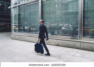 Side View Of Successful Middle Aged Man In Stylish Dark Business Suit Walking Down City Street With Big Dark Blue Bag In New York