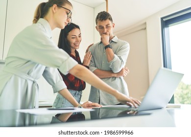 Side View Of Successful Realtor Woman Showing Clients Apartment Lease Agreement. Focused Woman Realtor In Glasses Typing At Laptop Keyboard, Draws Up A Lease Agreement For Tenants, Young Family Couple