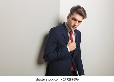Side view of a successful young business man leaning on a grey wall while fixing his tie.