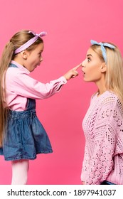 Side View Of Surprised Kid Touching Nose Of Mother Isolated On Pink