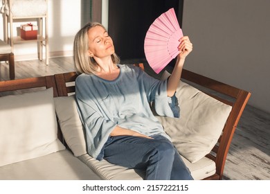 Side View Sweaty Middle Aged Lady Using Paper Waving Fan, Suffering From High Temperature Inside. Unhappy Middle Aged Woman Feeling Unwell, Cooling Herself At Home With No Air Conditioning System.
