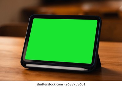 A side view of a tablet device with a blank green screen on the table