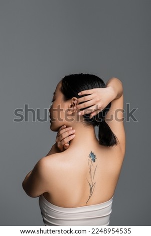 Side view of tattooed asian woman touching hair isolated on grey