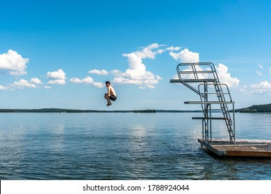 Side View Of A Teenage Male Jump Diving From A Diving Tower With Blue Sky And Horizon In The Background.