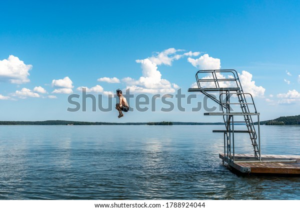 Side view of a teenage\
male jump diving from a diving tower with blue sky and horizon in\
the background.
