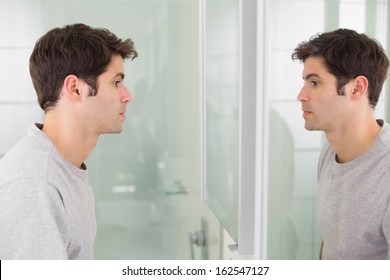 Side view of a tensed young man looking at self in mirror in the bathroom