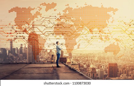 Side view of a thoughtful businessman standing on the rooftop of a skyscraper looking over the big city at sunset with a world map hologram projection. Cryptocurrency concept. Double exposure.