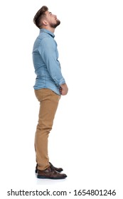 Side View Of A Thoughtful Casual Man Looking Up And Wondering, Standing On White Studio Background