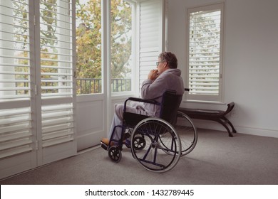 Side view of thoughtful disabled active senior Caucasian man looking through window on wheelchair in a comfortable home - Powered by Shutterstock