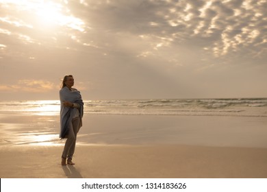 Side view of a thoughtful senior Caucasian woman wrapped in a shawl standing on the beach - Powered by Shutterstock