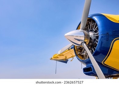 Side view of a three blade propeller and a radial engine on a yellow and blue airplane. Copy space off to the left.