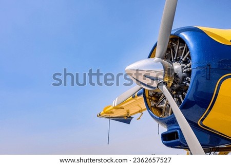 Side view of a three blade propeller and a radial engine on a yellow and blue airplane. Copy space off to the left.