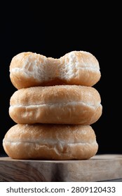 Side view of three delicious ring doughnuts stacked on a rustic wooden surface against a dark background