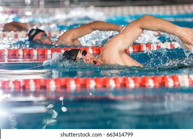 Side view of three male swimmers doing free style in different swimming lanes