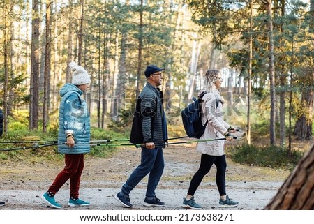 Side view of three people with backpack make Scandinavian, Nordic walking one by one, hold trekking sticks as team group in forest. Stepping technic for good posture. Healthy exercise education