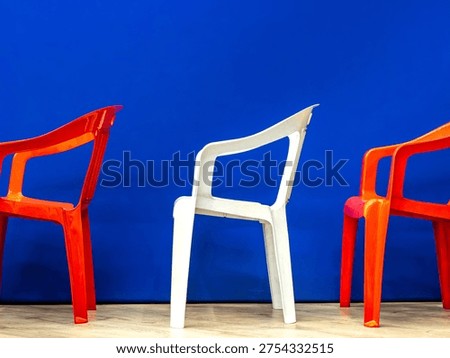 Side view of three plastic armchairs arranged in row r with red chairs flanking white center chair against blue backdrop demonstrating lightweight portable event seating solution, selective focus
