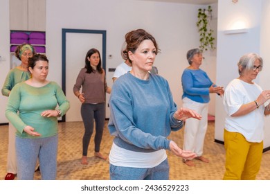 Side view three quarter length photo of a group of a mature adult women moving coordinated join hands in a qi gong class - Powered by Shutterstock