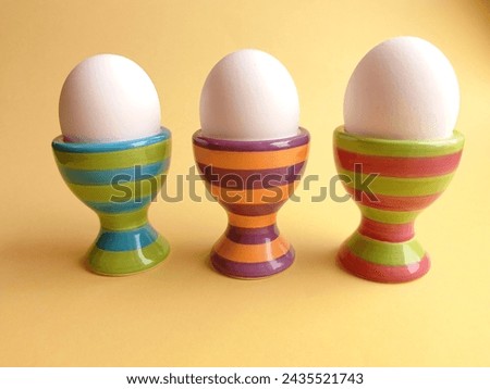 Side view of three white eggs in striped, colorful egg cups on the yellow background.