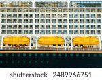 Side view of three yellow lifeboats and cabins balconies on a large multi-deck cruise ship, sea voyage safety equipment