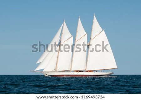 Side view of three-masted authentic windjammer or schooner passing by on a summer day with blue sky. Windjamming is a popular attraction in New England for the tourism industry.