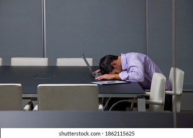 A side view of a tired businessman sleeping with his head rested on a laptop in the conference room