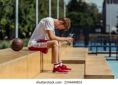 side view of tired sportsman sitting with sports bottle near ball - Powered by Shutterstock