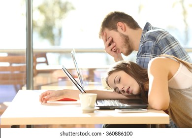 Side view of tired students surrendering to fatigue studying with laptops in a coffee shop with a window in the background and sky outdoors