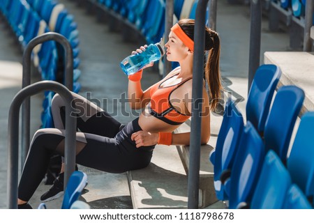 side view of tired young woman drinking water on stairs at sports stadium