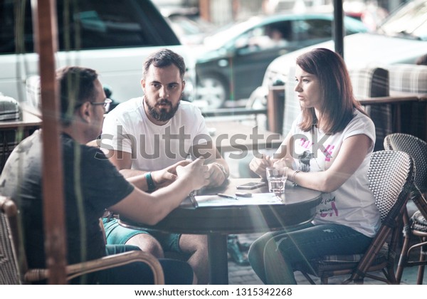 Side view and top. The company of three\
businessmen are discussing at the table in coffee, writing in a\
notebook, looking at a laptop, satkan with water, car keys,\
magazines, a smartphone,\
online.