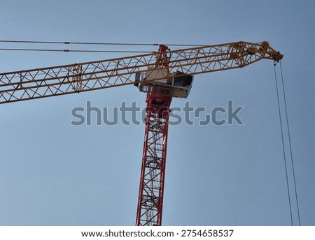 Side view of a tower crane operator cabin during assembly, with the lattice fly jib of a 450-ton mobile crane in the foreground.