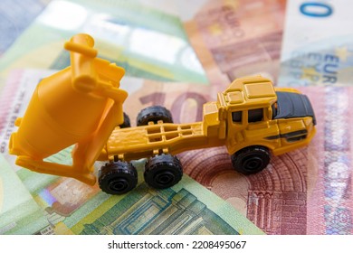 Side View Of A Toy Concrete Mixer On The Background Of Different Euro Banknotes. The Concept Of Expensive Modern Construction.