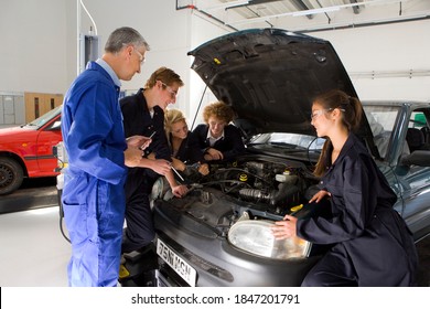 A Side View Of A Trainer Standing In Front Of A Car With Open Hood As He Watches His Students Repair It In A Vocational School Of Automotive Trade