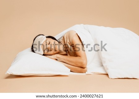 Side view tranquil happy young calm Latin woman she wearing pyjamas jam sleep eye mask rest relax at home lay down under duvet isolated on plain pastel beige background. Good mood night nap concept