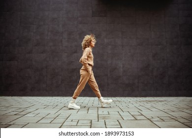 Side view of trap girl in tracksuit walking with hands in her pockets and listening music.