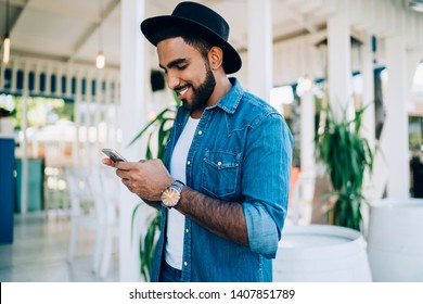 Side View Of Trendy Turkish Man In Black Hat Typing Text Sms For Sending To Favourite Blogger From Social Networks Connecting To 4g Wireless On Cellphone, Happy Cheerful Man Search Phone Number