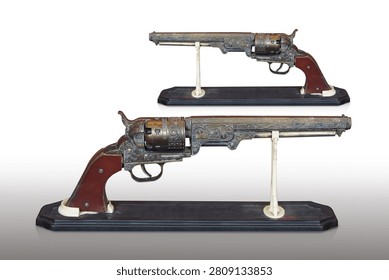side view two antique and old brass guns with a brown leather grip, placed on a wooden stand against a white background