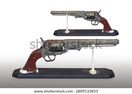 side view two antique and old brass guns with a brown leather grip, placed on a wooden stand against a white background