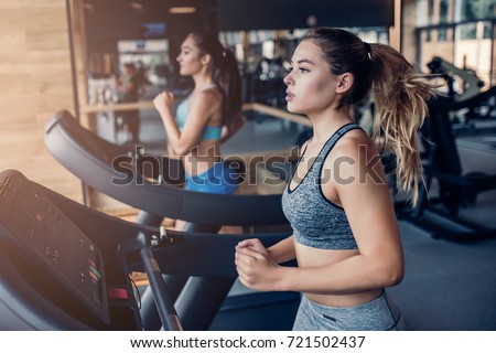 Side view of two attractive sports women on running track. Girls on treadmill